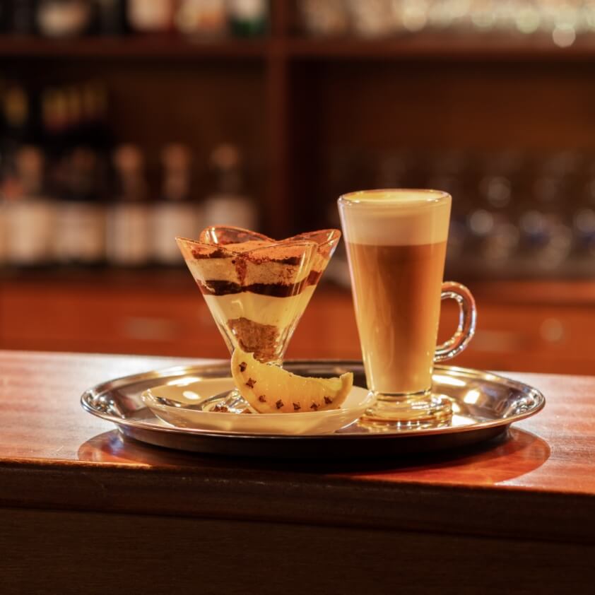 W oddali bar kawiarni na pierwszym planie szklanka z kawą oraz deserem