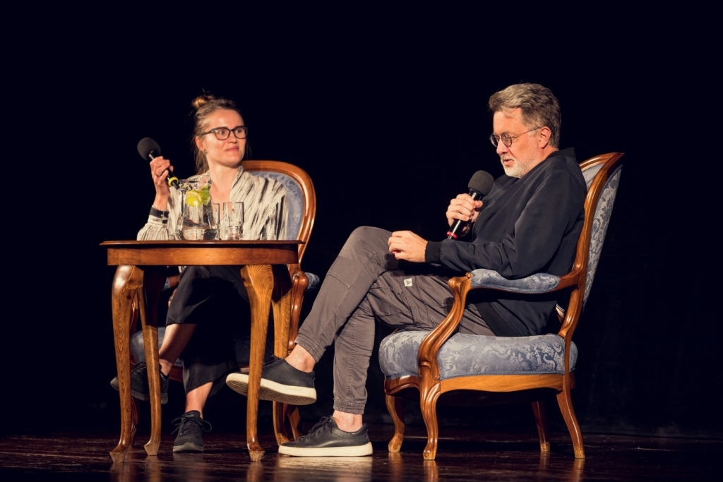 Na scenie przy stoliku siedzi mężczyzna i kobieta